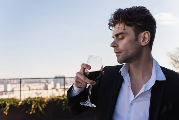 elegant man in suit holding glass of red wine outdoors - Foto, Bild