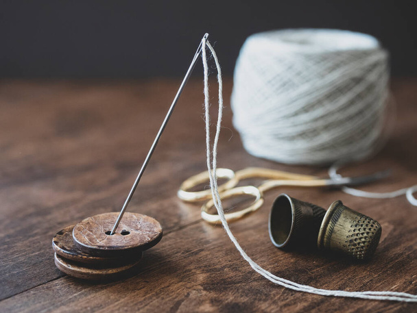 Pile of wooden buttons, needle, old thimbles, scissors and a cotton thread reel on the table. Concept of needlecraft, sewing, tailoring - Fotografie, Obrázek
