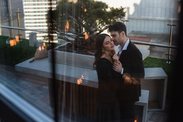 mujer y hombre abrazándose en la terraza detrás de la ventana borrosa del restaurante  - Foto, imagen