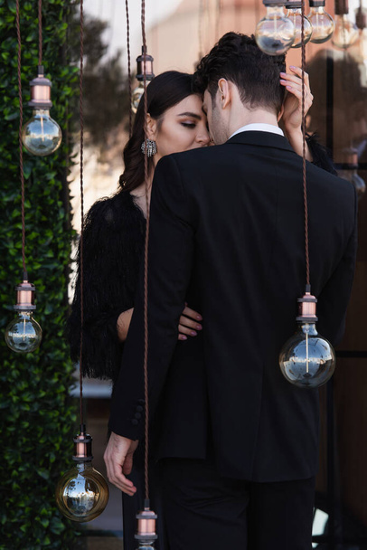 elegant woman hugging with man near light bulbs on terrace - Foto, Imagem
