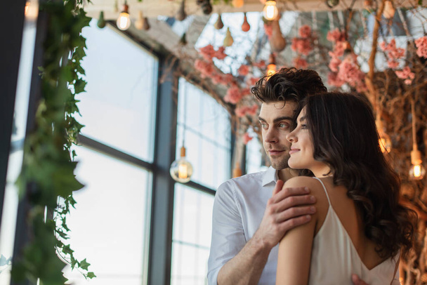 man and woman smiling while looking away and hugging in restaurant  - Photo, Image