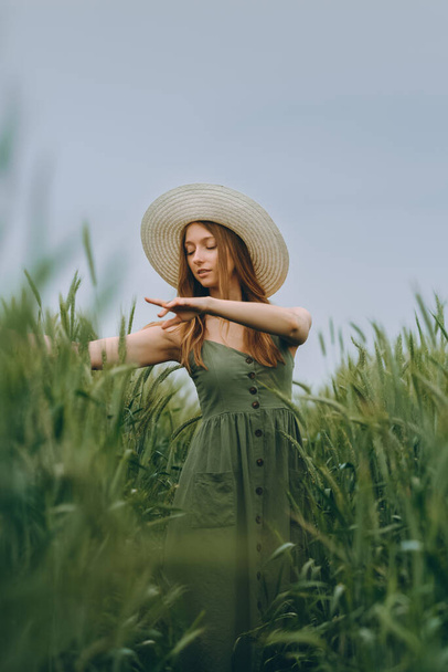 Şapkalı genç bir kadın buğday tarlasında yürüyor, hayattan ve yazdan zevk alıyor. Buğday tarlası. Güneş ışığı altında güzel doğa manzarası. Sağlıklı yaşam tarzı kavramı. Gürültülü görüntü, film tahılı - Fotoğraf, Görsel