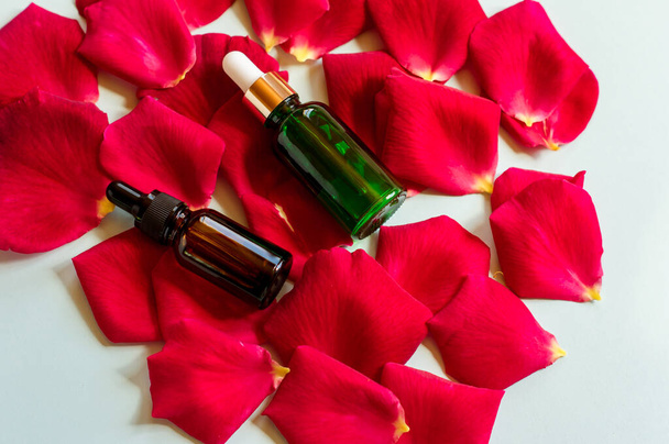 Homemade skincare natural rose water, essential oil product. Red rose petals and cosmetic glass bottle with dropper for moisturizing serum, facial toner, cleansing, makeup remover or treat acne - Фото, зображення