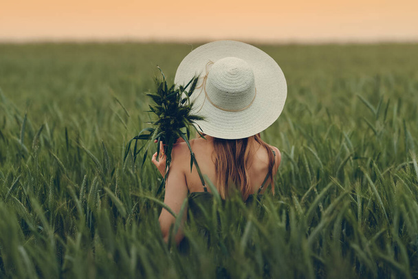Sahada gün batımına bakan genç bir kadın. Buğday tarlası. Güzel Doğa Günbatımı Manzarası. Olgunlaşan çayırlık buğday tarlalarının arka planı. Zengin hasat konsepti. Gürültülü görüntü, film tahılı - Fotoğraf, Görsel