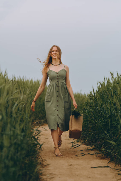 Mujer joven caminando en un campo de trigo, disfruta de la vida y el verano. Campo de trigo. Hermoso paisaje natural bajo la luz del sol. Concepto de estilo de vida saludable. Imagen con ruido, grano de película - Foto, imagen