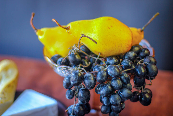 Прекрасная еда: темные виноградные кисти, кусочек сыра бри, два куска багета и несколько спелых жёлтых груш - Фото, изображение
