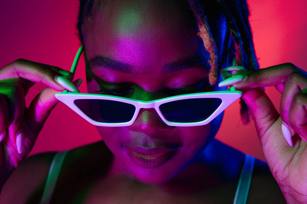 Schöne junge Afrikanerin mit stylischer Sonnenbrille auf blauem Hintergrund. - Foto, Bild