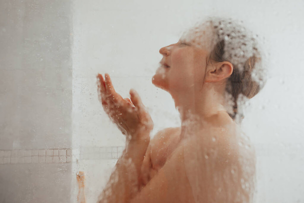 Showering woman behind glass door with water drops - Фото, зображення