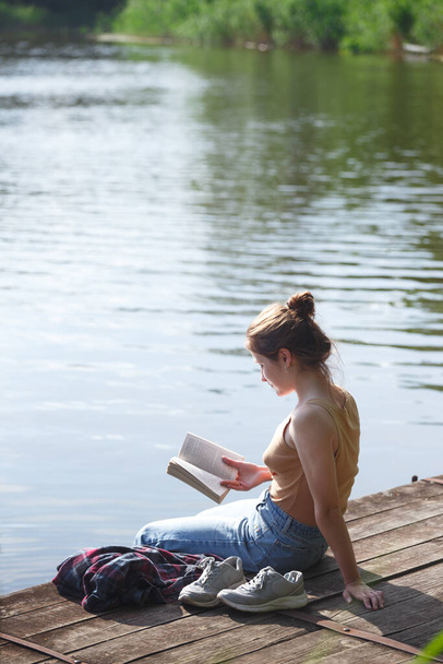 girl sitting on the pier and reading a boo - Foto, afbeelding