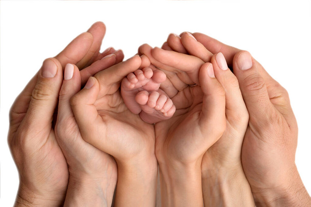 De handen van moeder, vader en ouder kind houden de voeten van de pasgeborene vast. Schattig familieportret met baby. Op een zwarte studio achtergrond. - Foto, afbeelding