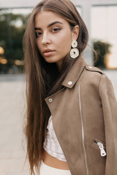 Close up portrait of spectacular lady with long hair wearing brown jacket and gold earnings looking at camera . High quality photo - Photo, Image