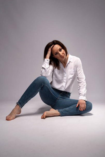 Giovane donna in camicia bianca e jeans in posa su sfondo grigio. Donna elegante. - Foto, immagini