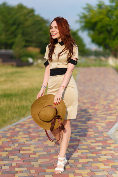 A happy young woman, holding a wide hat, poses in a park in summer - Foto, imagen