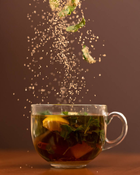 Herbal vitamin tea. Ingredients falling into glass cup with drink. Close up shot in motion on brown background. Side view. Soft focus - Photo, Image