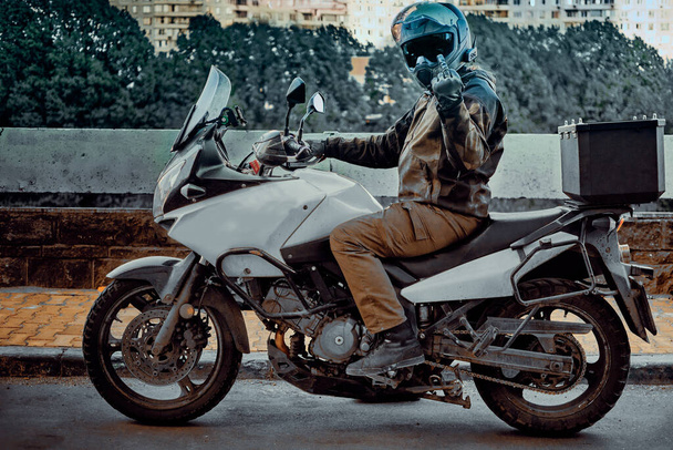Een motorrijder maakt een obsceen gebaar met zijn middelvinger. Aan hem een spiegelhelm - Foto, afbeelding