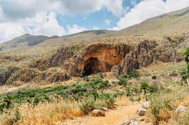 Large cave Grotta dell Uzzo in Zingaro Nature Reserve,Sicily,Italy.Important Prehistoric site with human remains.Landscape with entrance to huge karst cave.Famous landmark of Sicilian coast. - Photo, Image