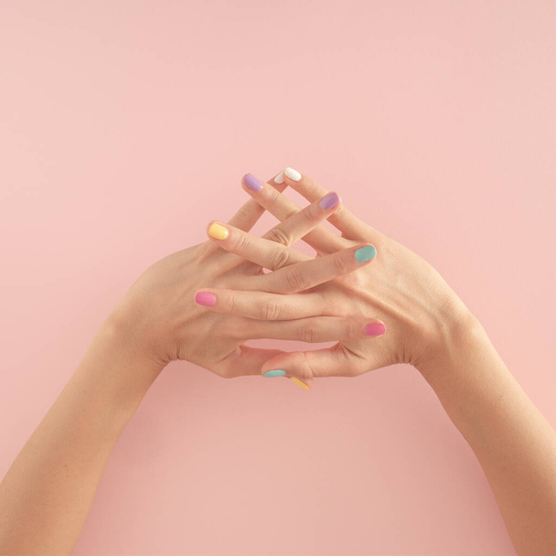 vrouwen handen met kleurrijke nagels op de pastel roze achtergrond. kopieer ruimte. zomer moderne tropische abstracte kunst met vrouwelijke hand. minimaal achtergrondidee met kopieerruimte - Foto, afbeelding