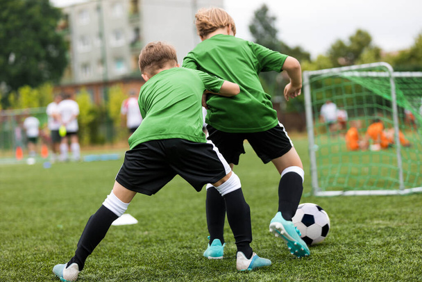 Futbol antrenmanında iki erkek çocuk yarışıyor. Okul futbol sahasında antrenman yapan mutlu çocuklar. Okul çocukları için yaz zamanı spor aktiviteleri - Fotoğraf, Görsel