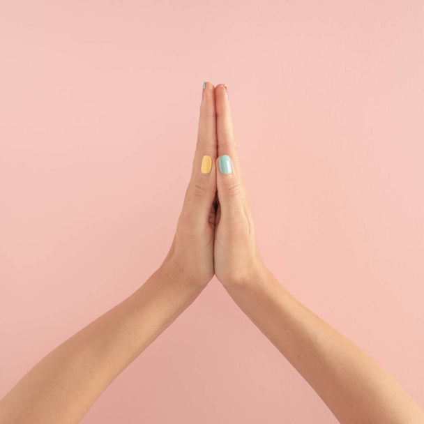 パステルピンクの背景にカラフルな爪を持つ女性の手。コピースペース。女性の手で夏の現代熱帯抽象アート。祈りを伴う最小限の背景の考え. - 写真・画像