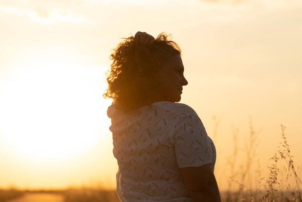 Dorosła kobieta cieszy się słońcem i dopasowuje swoje siwe włosy dłonią podczas spaceru po polu o zachodzie słońca, Hiszpania - Zdjęcie, obraz