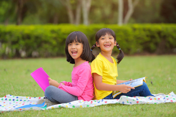 Słodka dziewczynka czytająca książki na trawie. Ma spojrzenie przyjemności na twarzy i wygląda na bardzo zrelaksowaną. Co zwiększa rozwój i zwiększa umiejętności uczenia się poza pomieszczeniem. - Zdjęcie, obraz
