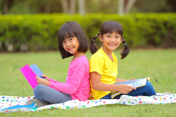 Cute little girl  reading books on the grass. She has a look of enjoyment on her face and she looks very relaxed. Which increases the development and enhances learning skills outside the room. - Photo, Image