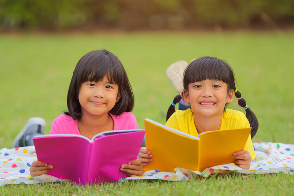 Nettes kleines Mädchen liest Bücher auf dem Gras. Sie hat einen genussvollen Blick auf ihr Gesicht und sieht sehr entspannt aus. Das steigert die Entwicklung und verbessert die Lernfähigkeit außerhalb des Raumes. - Foto, Bild