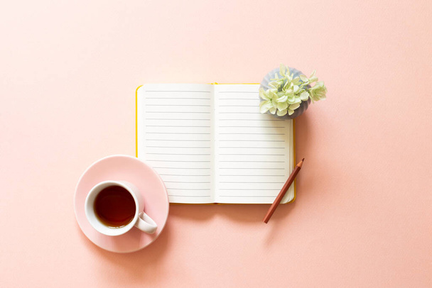 Offenes Notizbuch, Tasse Tee, trockene Blumen auf rosa Hintergrund. Alltag, Arbeitsplatz, Studienkonzept - Foto, Bild