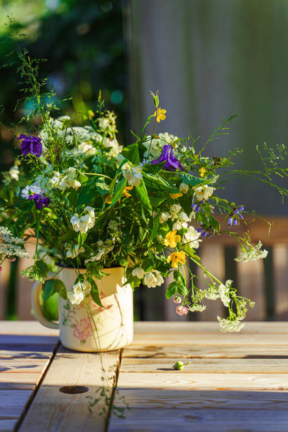 Virágcsokor mezei virágokkal a kerti asztalon, napsugarakkal megvilágítva.  - Fotó, kép
