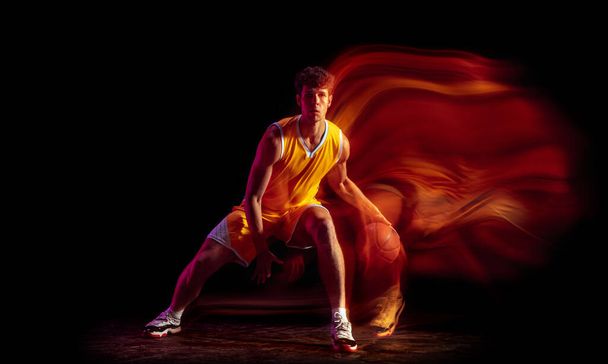Young Caucasian professional basketball player exercising isolated on black background in mixed neon lights. - Foto, immagini