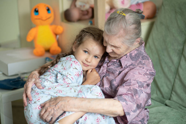 Yaşlı bir kadın ve küçük bir kızın portresi, büyükannesi torununa sarılıyor, aile bağları, yaşlılık ve gençlik, 90 yaşında, yaşlı bir yüzdeki kırışıklıklar, güzel bir yaşlılık, bir kadın ve bir çocuk. - Fotoğraf, Görsel