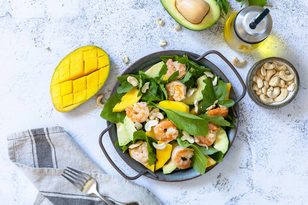 Healthy diet salad with arugula, spinach, mango, avocado, shrimp, pecans and vinaigrette dressing on a gray stone table top. Top view flat lay background. - Foto, imagen