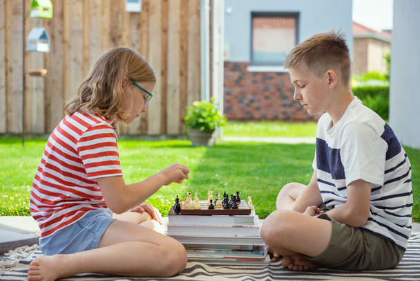 Two happy children playing chess on backyard at sunny day while summer holidays - Foto, afbeelding