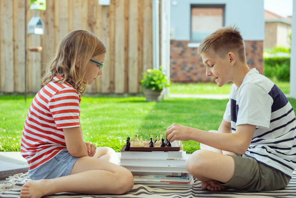 Two happy children playing chess on backyard at sunny day while summer holidays - Fotoğraf, Görsel