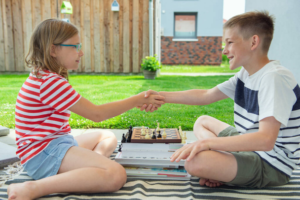 Two happy children playing chess on backyard at sunny day while summer holidays - Photo, image