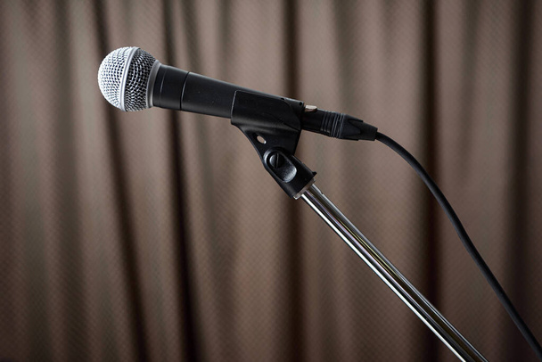A gray microphone on a stand stands on the stage against the background of a brown curtain. - Фото, изображение