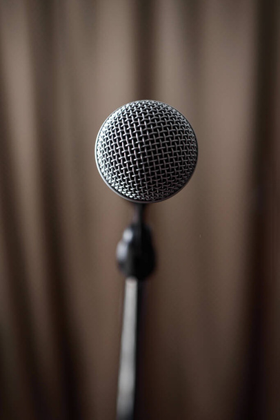 Un microphone gris sur un support se tient sur la scène sur le fond d'un rideau brun. - Photo, image