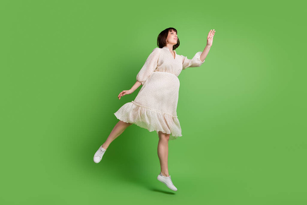 Longitud completa cuerpo tamaño foto mujer usando vestido de glamour punteado saltando buscando copyspace aislado pastel verde color fondo - Foto, imagen