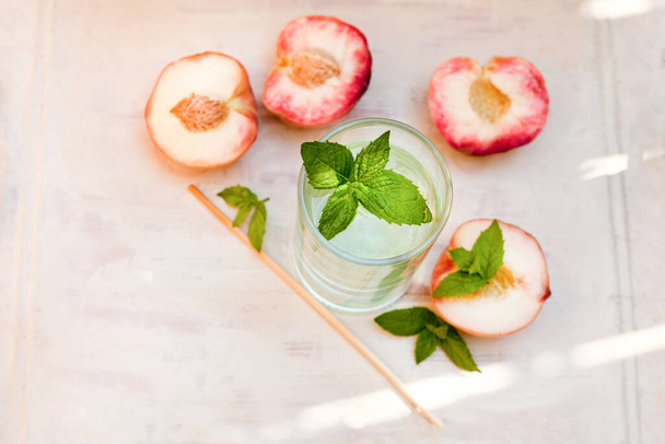 Wassergetränk mit Pfirsichen - erfrischender Eistee mit Pfefferminze und Pfirsichen auf grauem Hintergrund, selektiver Fokus. - Foto, Bild