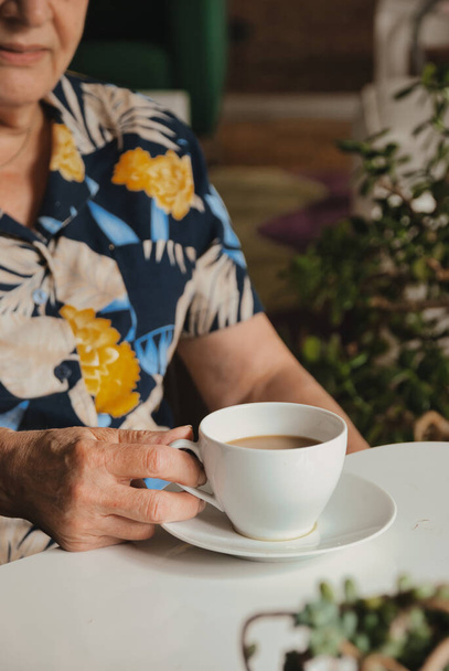 Oudere vrouw met koffiebeker aan tafel - Foto, afbeelding