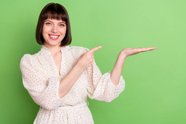 Fénykép a fiatal lány boldog pozitív mosoly pont ujjak termék promo reklám elszigetelt zöld színű háttér - Fotó, kép