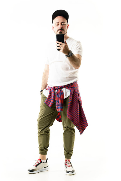 Cool modern városi stílusban fiatal férfi fotózás okos telefon visel sapkát. Teljes test portré elszigetelt fehér háttér - Fotó, kép
