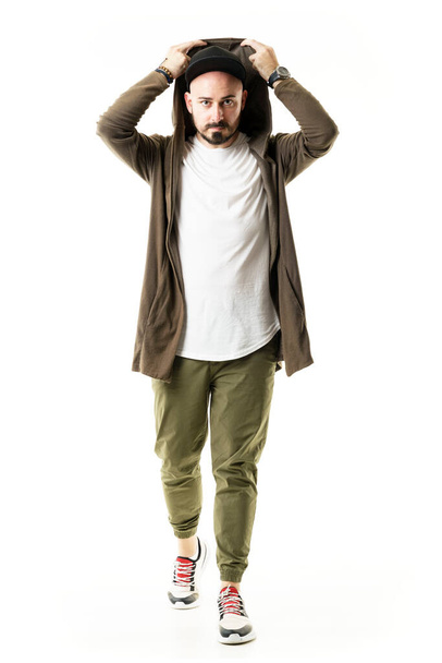 Stylish modern urban young man wearing cardigan put on hoodie walking towards camera. Full body portrait isolated on white background - Фото, зображення
