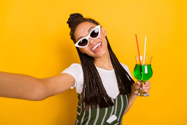 Photo of positive young dark skin woman make selfie camera hold cocktails isolated on yellow color background - Foto, imagen