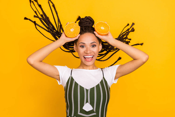 Photo of funny excited dark skin lady wear striped clothes holding head orange fruit smiling isolated yellow color background - Zdjęcie, obraz