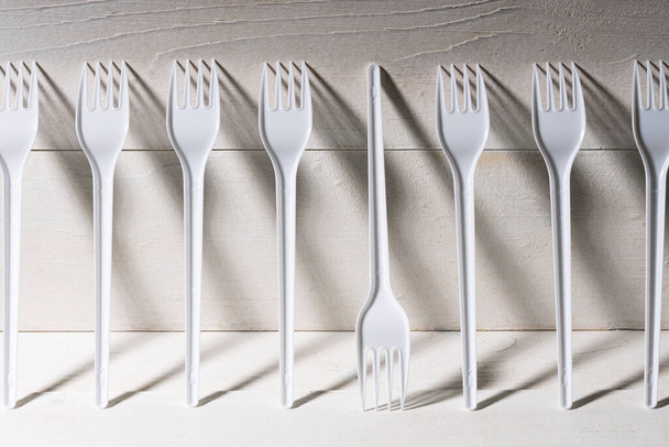 a row of forks standing against the wall, one of them upside down and different from the others. shadows and light on plastic forks - Photo, Image