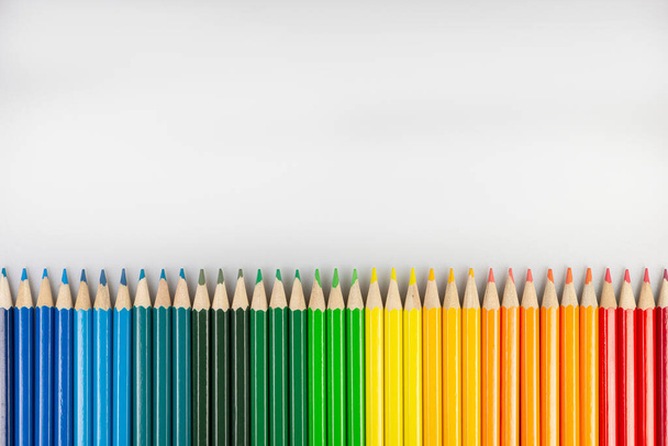 Rij van ceder gekleurde potloden op een horizontaal wit papier - Foto, afbeelding