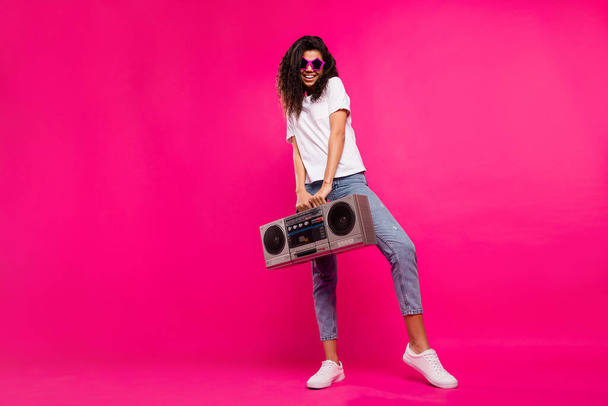 Full length photo of crazy millennial lady hold boom box wear spectacles t-shirt jeans sneakers isolated on pink background - Фото, зображення