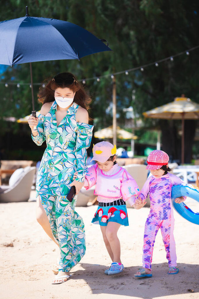 Image verticale. Beau portrait de voyage en famille sur la plage. Mère et fille marchent sur le sable. Anneau en caoutchouc pour enfant. Maman a mis un parapluie à l'abri du soleil. Heure d "été. - Photo, image