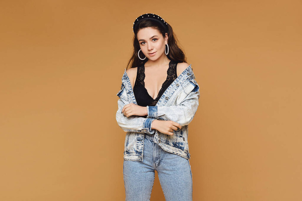 Caucasian young woman with wavy hair in denim clothes, isolated on beige. Model girl in a modish outfit at the beige background - Valokuva, kuva